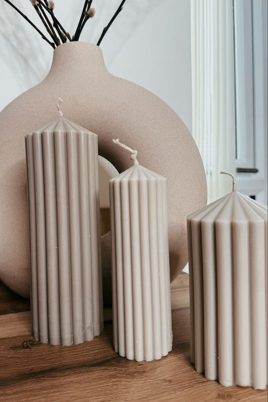 Set of beige candles and a large round vase on a wooden surface.